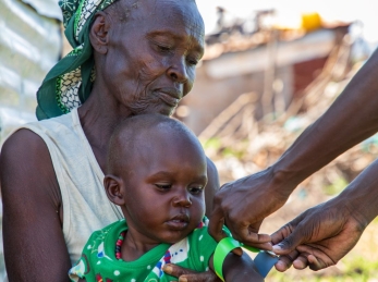 Mother holding a child while an aid worker measures the child's malnutrition level