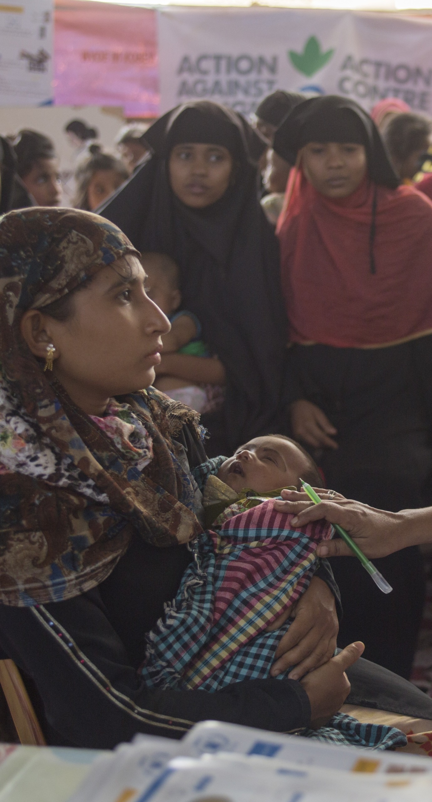 Health education officer, Shaki Rani Bose, talks to a young mother, Hosne Ara, with her baby, surrounded by Rohinga women as they wait patiently to be seen at an Action Against Hunger clinic for pregnant and breastfeeding mothers.