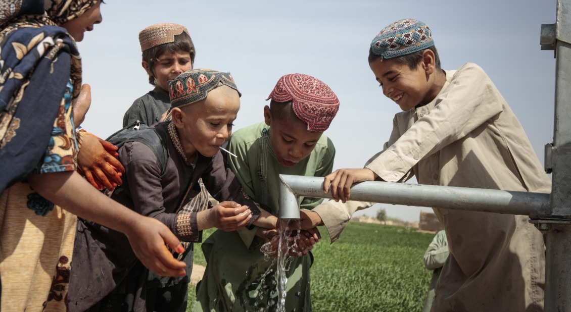 School-age children play with water from a pump.