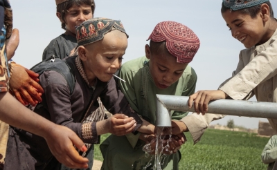 School-age children play with water from a pump.