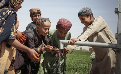 School-age children play with water from a pump.