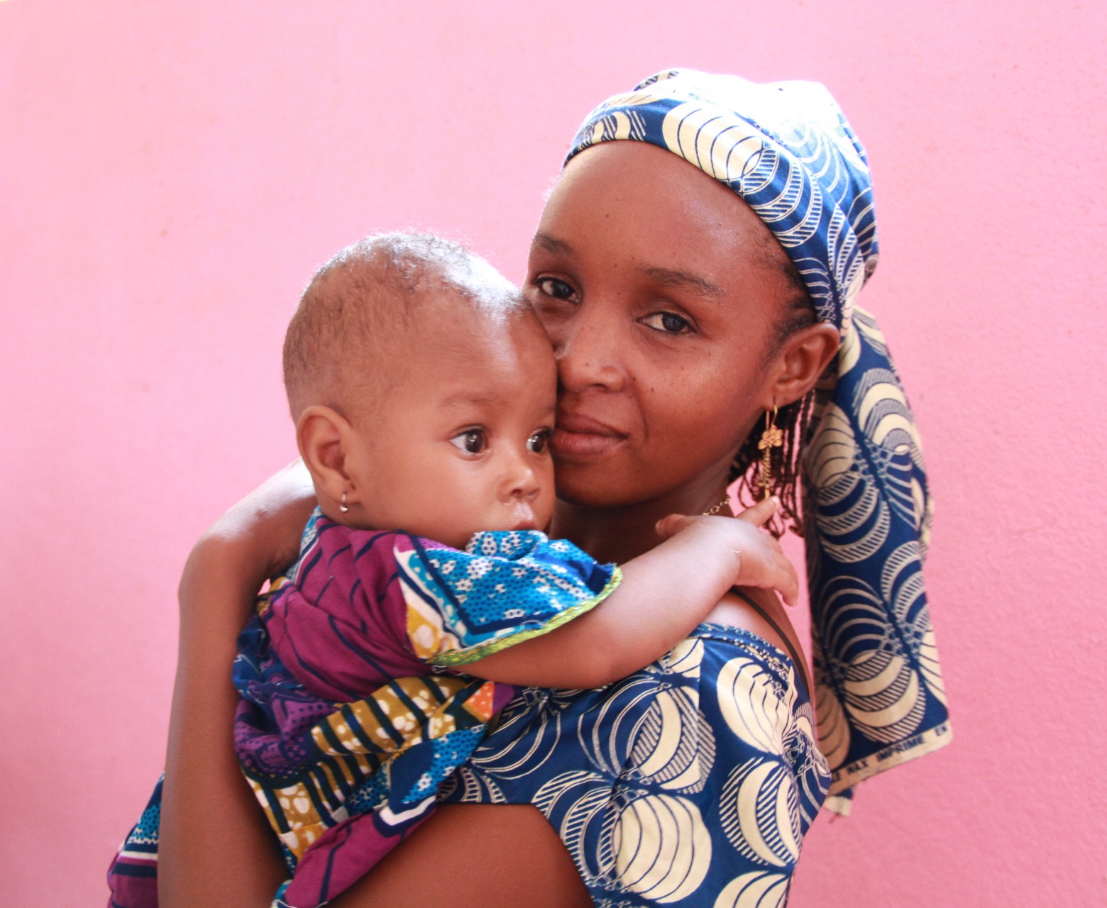 A mother and child in front of a pink wall in Cameroon.