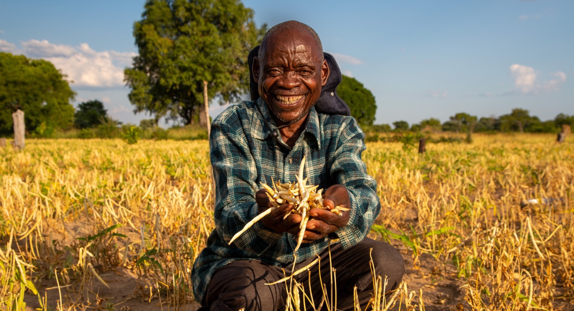 Farmer Sitwala Mangolwa (66) holds a handful of cowpeas whilst smiling at the camera on his farm in Siwela Village, Ngundi Camp