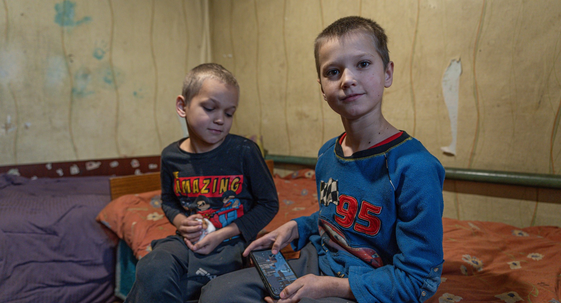 Two Ukrainian children sitting on a bed.
