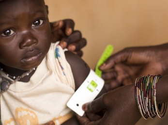 A health worker measures a child's upper arm with a color-coded band that is used to detect malnutrition.