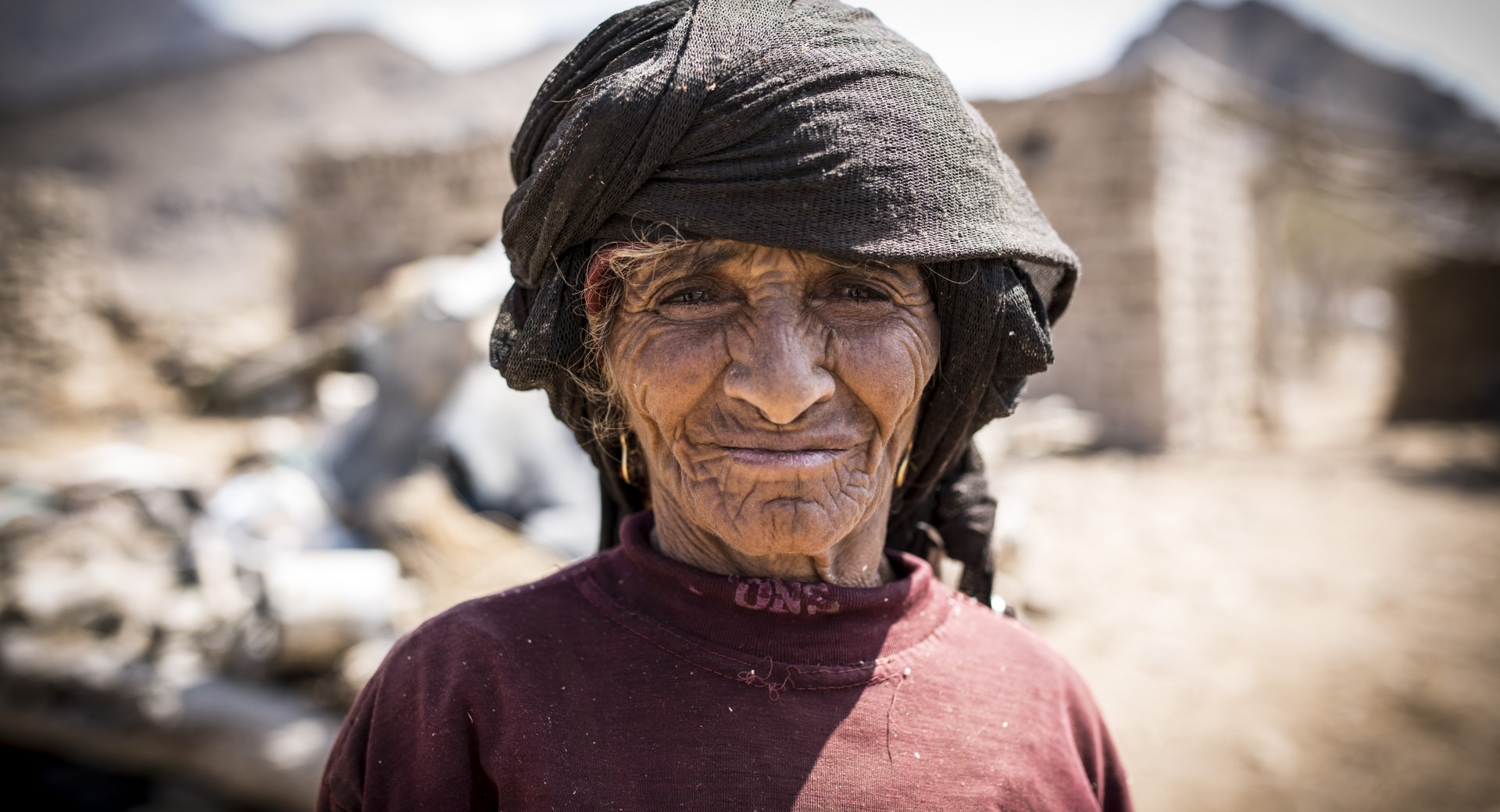 In Yemen, a woman stands in front of her community, which has been destroyed by conflict.
