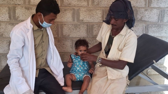 A healthcare worker helps a child next to their parent in Yemen.