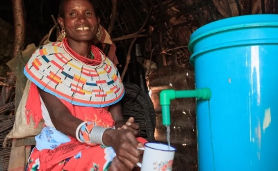 A woman in Kenya using a drinking water filter, pouring water into a cup.